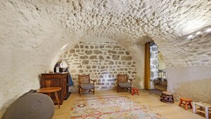 Ambiente interno con parete in pietra, mobili in legno, tappeto decorato e un piccolo sgabello.