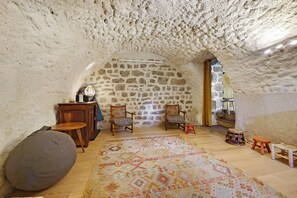 Un intérieur avec un mur en pierre, des meubles en bois, un tapis à motifs et un petit tabouret.