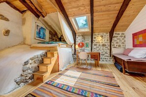A rustic room with a sloped ceiling, stone walls, a wooden bed, a desk, and a colorful rug.
