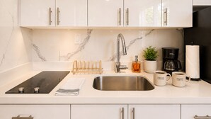 Een moderne keuken met witte kasten, een RVS spoelbak, een koffiezetapparaat en een waterkoker.