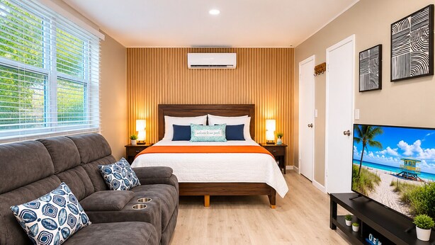 Een slaapkamer met een bed, een slaapbank, een televisie en een wandairconditioner.