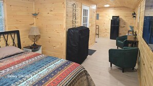 Quarto com painéis de madeira, uma cama, uma mesa, uma cadeira, um abajur e uma geladeira.