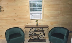 A wooden room with a window, a table with a figurine, and two green chairs.