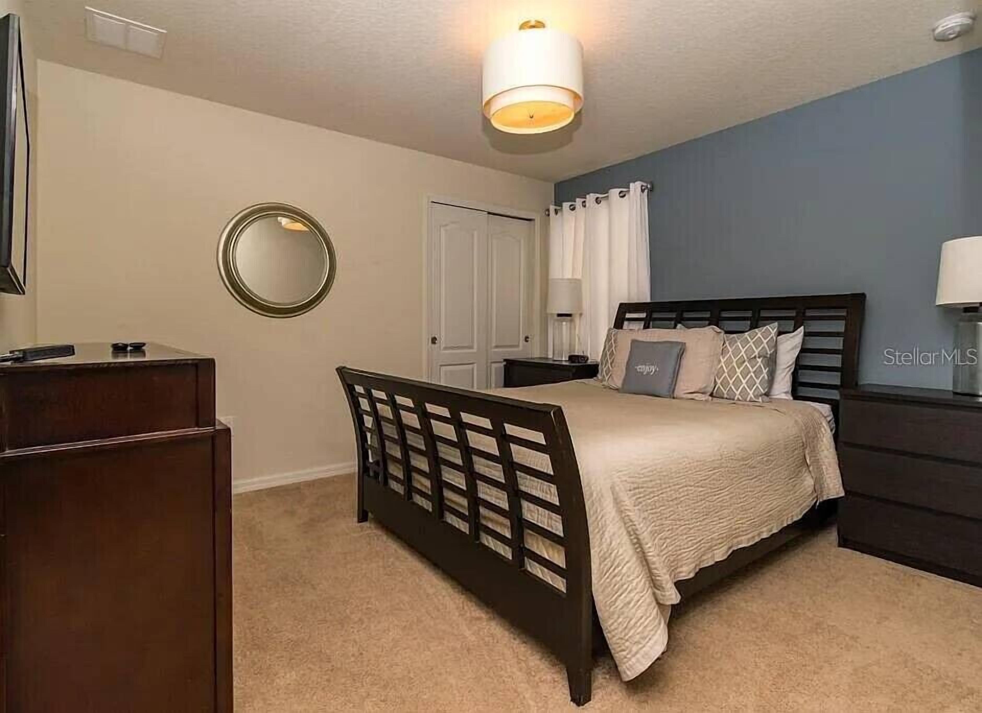 A bedroom with a bed, bedside table, lamp, and a mirror on the wall.