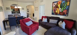 A living room with a red armchair, a dark brown sofa, and a dining area with a table and chairs. - Last Minute Disney Getaway! Luxury Condo with Private Balcony. Book Now! #173229 (Orlando)