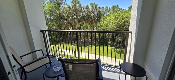 A balcony with a view of a grassy area and trees, equipped with two chairs and a small table. - Last Minute Disney Getaway! Luxury Condo with Private Balcony. Book Now! #173229 (Orlando)