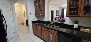 A kitchen with wooden cabinets, a black countertop, and a dishwasher. - Last Minute Disney Getaway! Luxury Condo with Private Balcony. Book Now! #173229 (Orlando)