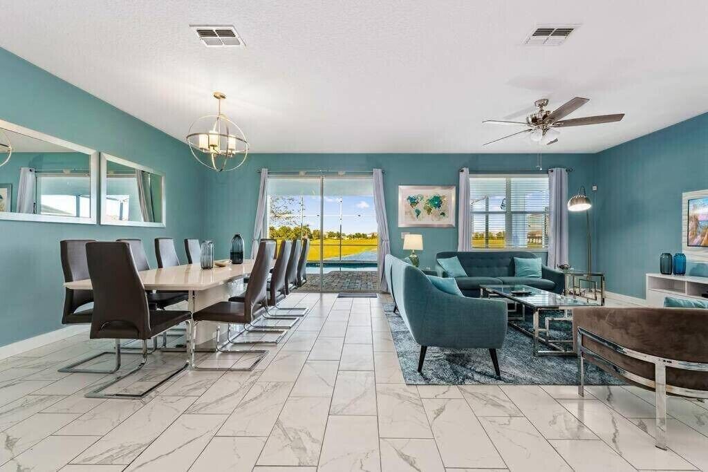 A modern living room with a dining area, large windows, and a ceiling fan.
