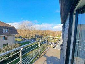 A balcony with a metal railing overlooking a residential area, a clear sky, and a distant view of trees and houses. - Spacious Family Stay in Oostduinkerke (Koksijde)
