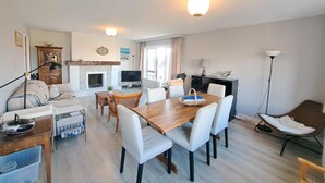 A living room with a fireplace, a dining table with chairs, a sofa, a TV, and a lamp. - Spacious Family Stay in Oostduinkerke (Koksijde)
