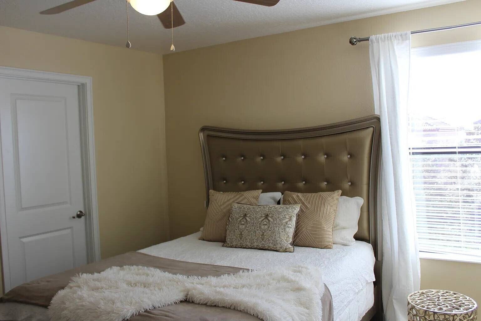 A bedroom with a bed, a ceiling fan, a window with curtains, and a door.