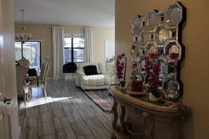 Ein geräumiges Wohnzimmer mit einem weißen Sofa, einem dekorativen Spiegel und Blick durch ein Fenster.