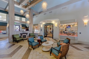 Eine geräumige Lobby mit hohen Decken, großen Fenstern und einer zentralen Sitzecke mit Korbstühlen und einem Couchtisch.