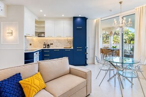 A modern living room with a sofa, a glass dining table, and a kitchen area with blue cabinets. - GuestReady - Modern comfort with garden and pool (Marbella)