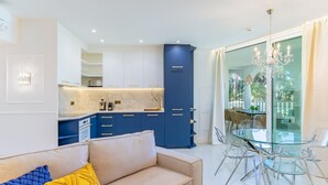Un salon moderne avec un canapé, une table à manger en verre et un coin cuisine doté de meubles bleus.