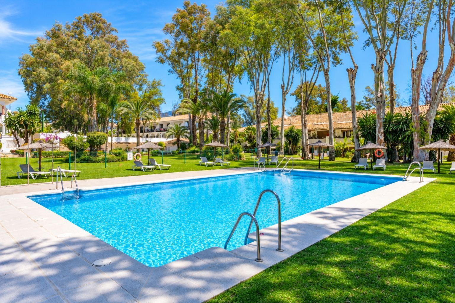A rectangular swimming pool with a clear blue water surface, surrounded by a well-maintained lawn and trees.