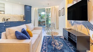 Un salon moderne avec un canapé, une table basse en verre, un téléviseur et une cuisine en arrière-plan.