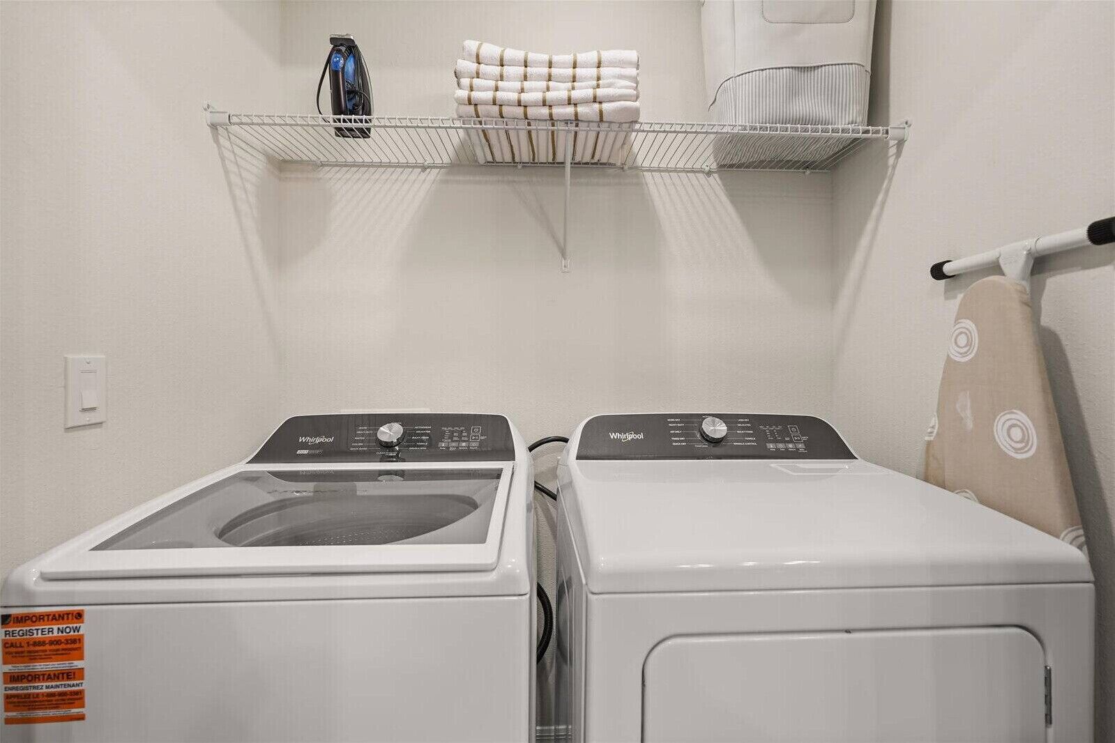 A laundry area with two front-loading washers and dryers, a shelf with folded towels, and a hairdryer on a stand.