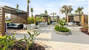 Un espace extérieur aménagé en terrasse, avec des coins salon, des zones abritées et des palmiers.