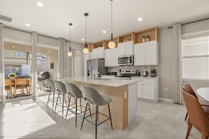 A modern kitchen with a central island, bar stools, and a dining area with a table and chairs. - Last Minute Disney Getaway! Private Pool, Game Room & Themed Bedrooms. Book Now! #161131 (Orlando)