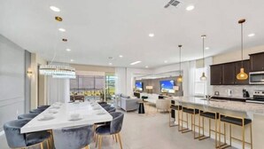 A modern kitchen with a long dining table, bar seating, and a TV. - Last Minute Disney Getaway! Private Pool, Game Room & Themed Bedrooms. Book Now! #173751 (Orlando)