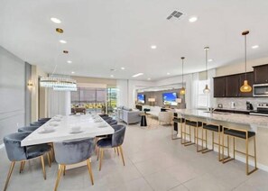 A modern kitchen with a long dining table, bar seating, and a TV. - Last Minute Disney Getaway! Private Pool, Game Room & Themed Bedrooms. Book Now! #173751 (Orlando)