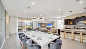 A modern kitchen with a central island, bar seating, and a dining area with a large table. - Last Minute Disney Getaway! Private Pool, Game Room & Themed Bedrooms. Book Now! #173751 (Orlando)