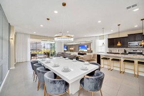 A modern kitchen with a central island, bar seating, and a dining area with a large table. - Last Minute Disney Getaway! Private Pool, Game Room & Themed Bedrooms. Book Now! #173751 (Orlando)