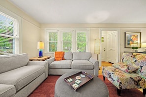 A living room with a grey sectional sofa, a patterned ottoman, and a colorful chair.