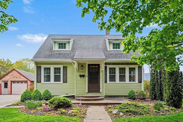 A two-story house with a front porch, a chimney, and a well-maintained garden.