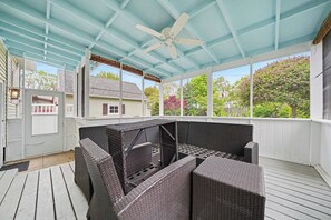 A covered porch with wicker furniture, a ceiling fan, and a view of a house and trees.