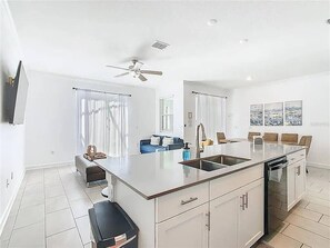 Eine moderne Küche mit Kochinsel, ein Essbereich mit Tisch und Stühlen sowie ein Wohnbereich mit Sofa und Fernseher.