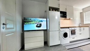 A compact kitchen with a washing machine, a microwave, and a television. - Newly built studio apartment (Gothenburg)