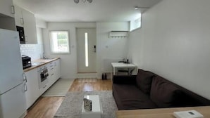 A compact kitchen with a refrigerator, oven, and sink. There is a small dining area with a table and a couch. - Newly built studio apartment (Gothenburg)