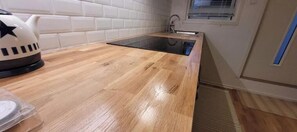 A kitchen with a wooden countertop, a black induction cooktop, and a kettle. - Newly built studio apartment (Gothenburg)