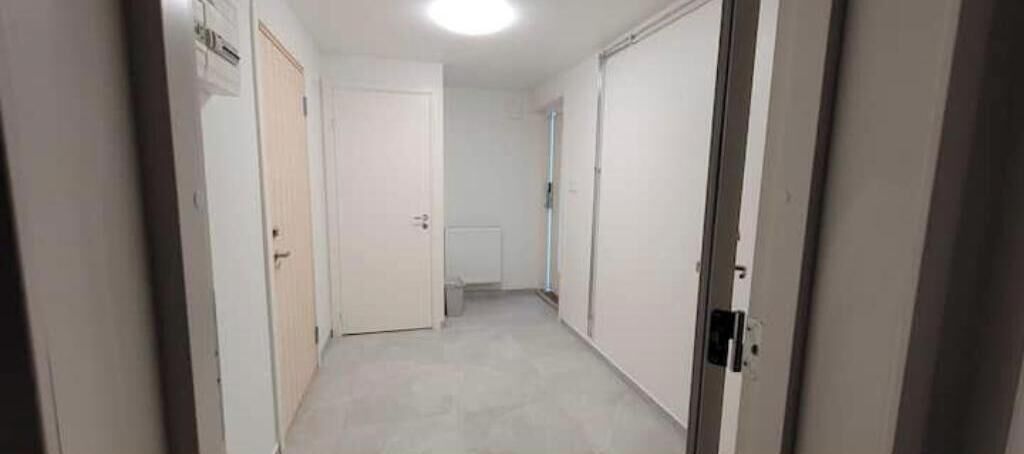 Un pasillo estrecho con puertas blancas, un radiador y una lámpara.