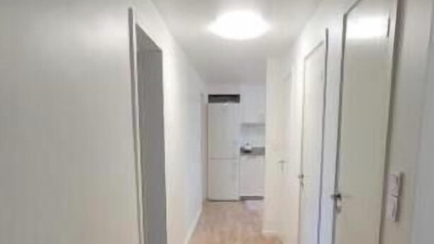 Un pasillo estrecho con suelo de madera, paredes blancas y puertas a ambos lados que dan a una zona de cocina.
