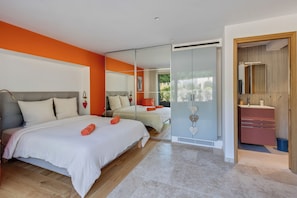 Ein modernes Schlafzimmer mit großem Bett, separatem Schlafbereich, Badezimmer mit Spiegel und Waschbecken sowie einer Glasschiebetür zu einem Balkon.