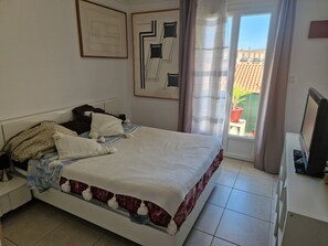 Ein Schlafzimmer mit Bett, Schreibtisch, Fernseher und einem Balkon mit Blick auf Gebäude.