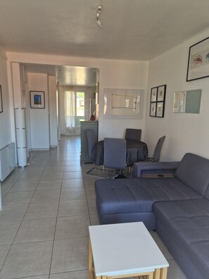 Ein modernes Wohnzimmer mit einem grauen Sofa, einem weißen Tisch und einer Küchenzeile im Hintergrund.