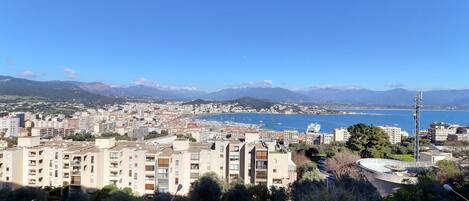 Paisagem costeira com edifícios residenciais, um porto de iates e montanhas ao fundo.