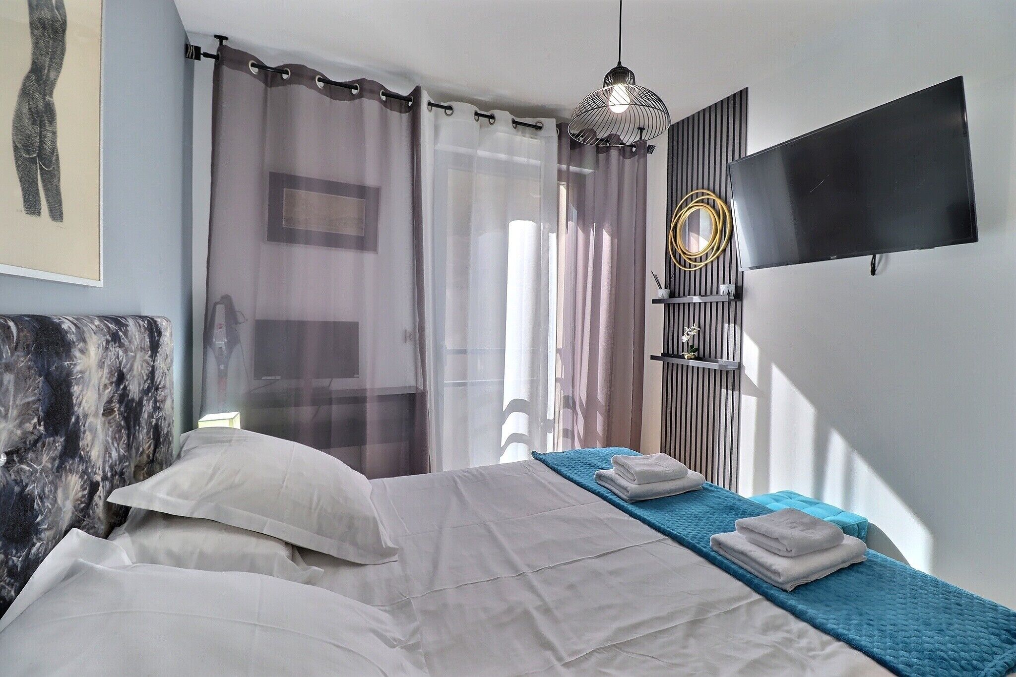 Un dormitorio con cama, cortinas, televisor y espejo fijado a la pared.