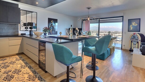 A modern kitchen with a central island, bar stools, and a large window offering a view. - Casa Simona - Vue mer incroyable (Ajaccio)