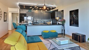 A modern living room with a sofa, ottoman, glass coffee table, and a kitchen area with a central island. - Casa Simona - Vue mer incroyable (Ajaccio)