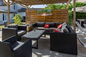 An outdoor patio with wicker furniture, a table, and a painting on the wall.