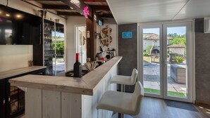 Un espace bar avec un comptoir en bois, des tabourets de bar blancs et une vue sur la terrasse extérieure.