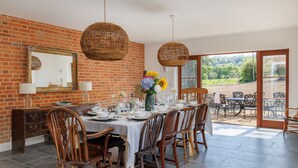 A dining area with a brick wall, wicker pendant lights, a table set for six, and a view of the outdoors. - The Farmhouse at Nunwell (Brading)