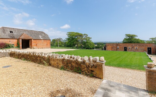 A rural property with a gravel driveway, a stone wall, and a grassy lawn.