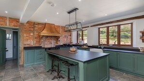 A kitchen with a large island, green cabinets, a brick wall, and a window with a view. - The Farmhouse at Nunwell (Brading)