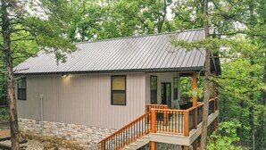 Une cabane avec un toit en métal, une terrasse en bois et des fondations en pierre.
